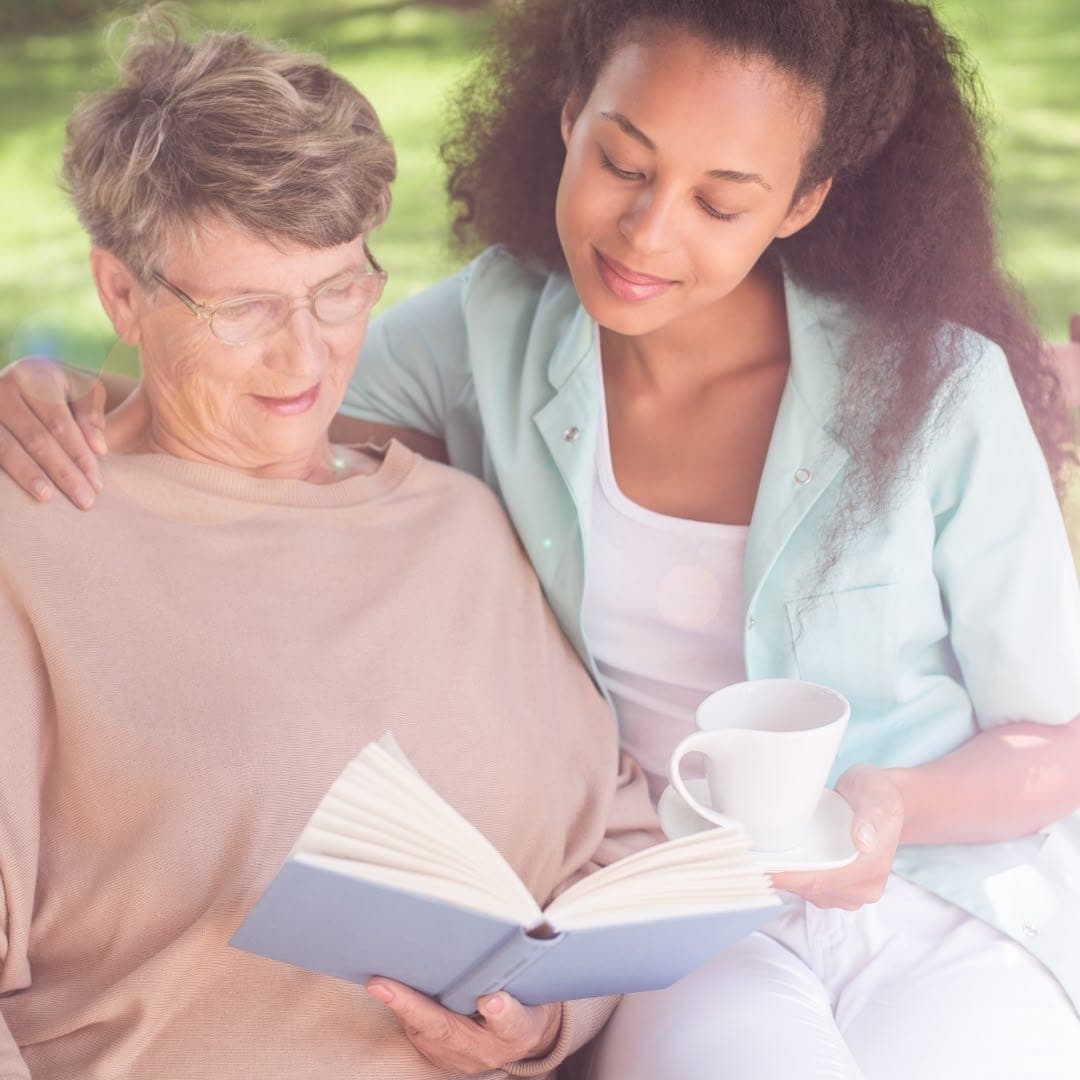 A younger woman sitting outdoors with an older woman, reading together