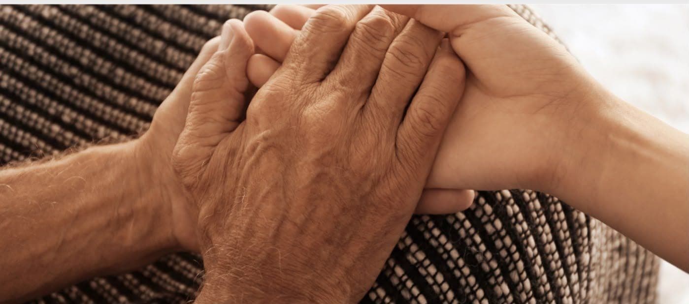 A pair of younger hands gently holding the hands of an older person